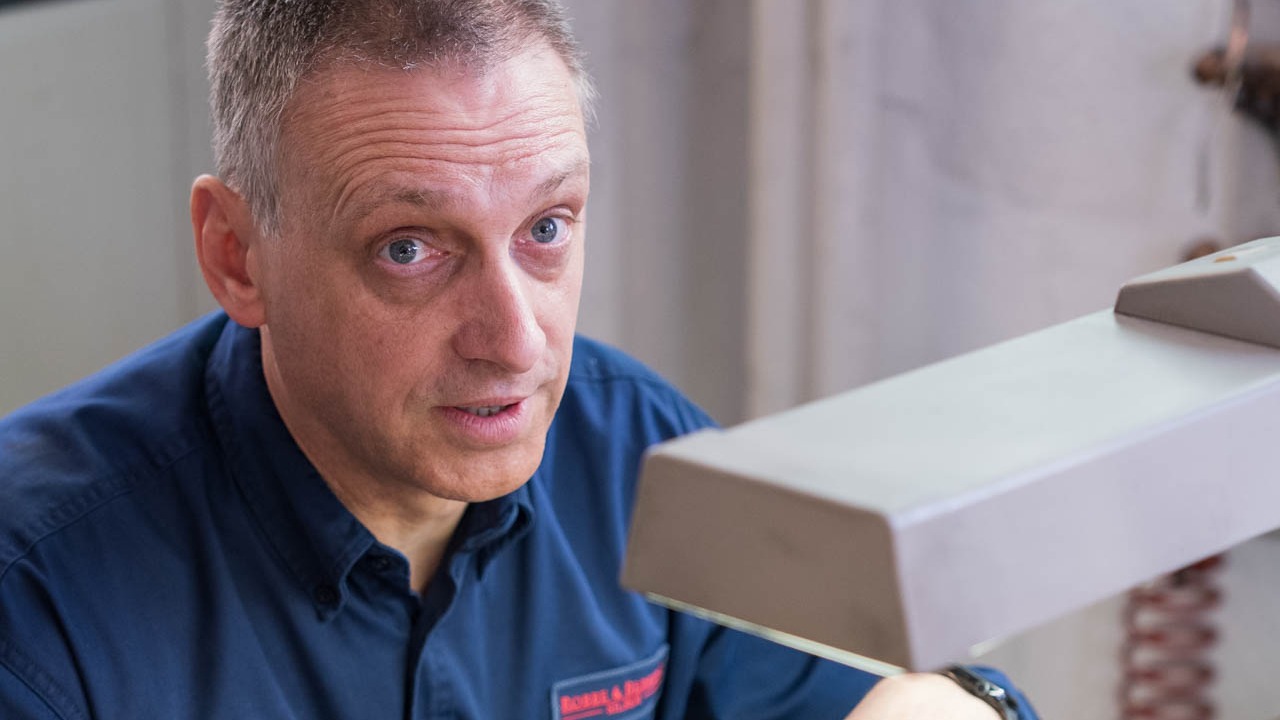 Ein Mann sitzt an einer Werkbank und schaut nach oben in die Kamera
